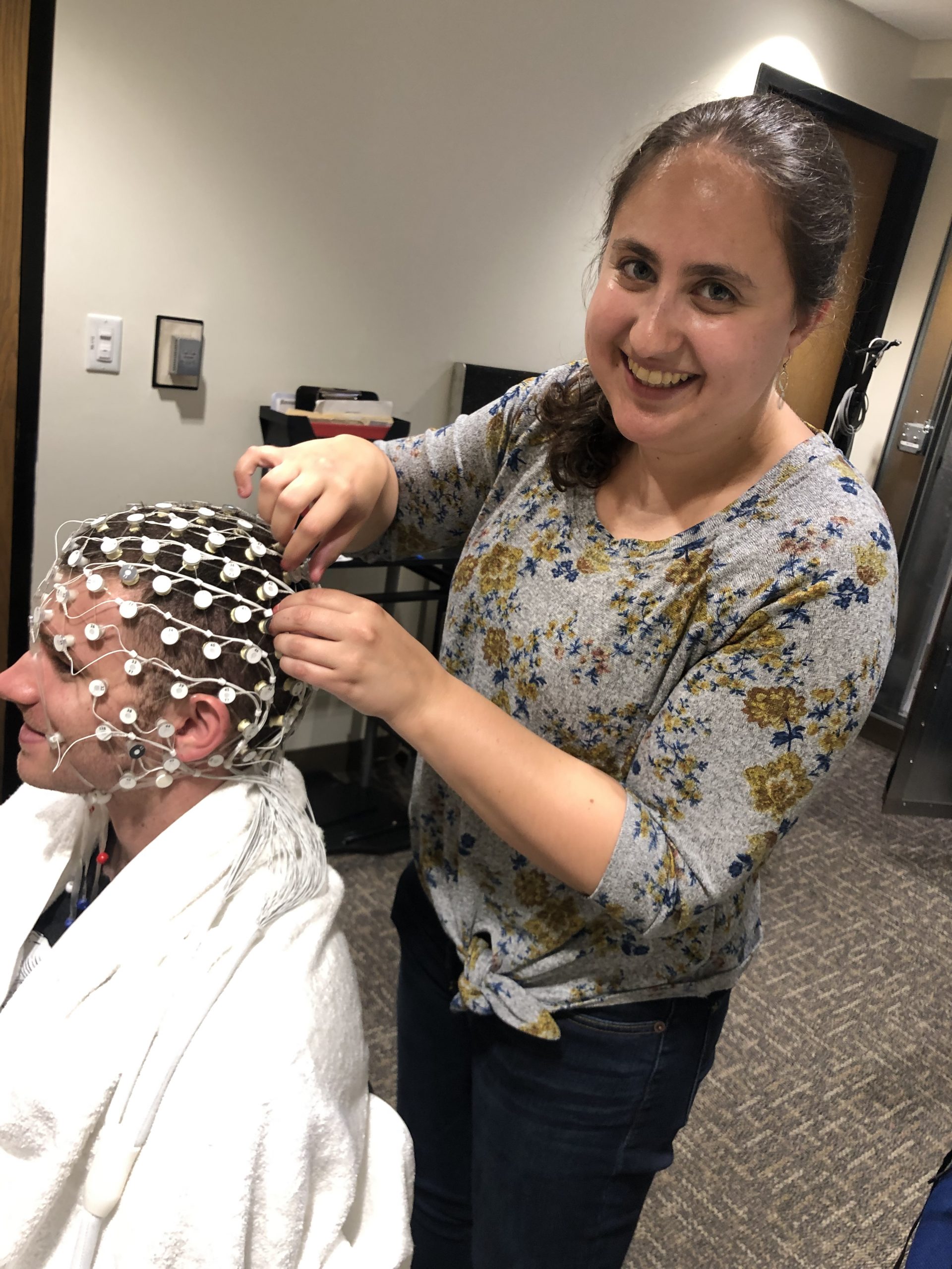 A picture of Arielle Keller placing an EEG electrode cap on a participant in a research lab